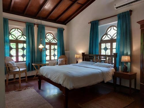 a bedroom with a bed with blue curtains and windows at Marbella Guest House in Sinquerim