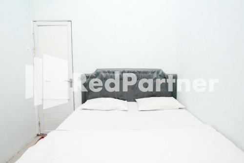 a bed in a white room with a mirror at Happy Inn Puspo Mitra RedDoorz in Jomblang