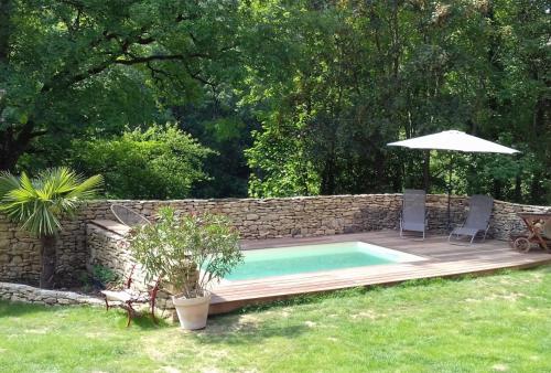 a swimming pool with an umbrella and a stone wall at Les Gîtes du Fraysse, au paradis des oiseaux in Montignac