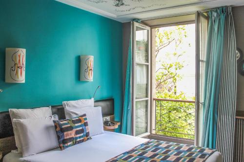パリにあるメルキュール パリ オペラ グラン ブールヴァールの青い壁のベッドルーム1室、ベッド1台、窓が備わります。
