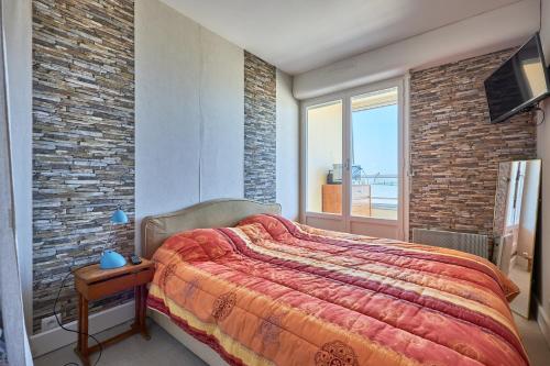 une chambre avec un grand lit et un mur de briques dans l'établissement La Longue Vue - Appt face à la mer, à Courseulles-sur-Mer