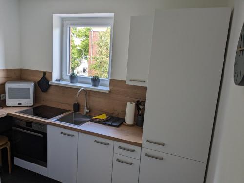 cocina con armarios blancos, fregadero y ventana en Ferienwohnung Auszeit, en Rostock