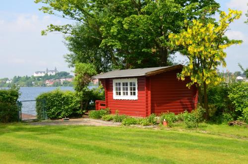a small red cabin in the grass near a lake at Ferienwohnungen Himmelsstübchen und Gartenstübchen in Plön