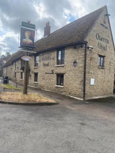 un bâtiment avec un panneau sur son côté dans l'établissement The Queens Head Inn, à Milton Ernest