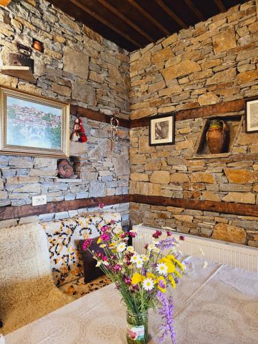 a room with a stone wall with a bed and flowers at Панорама хаус Лещен и еко къщи Дървена и Землянка in Leshten