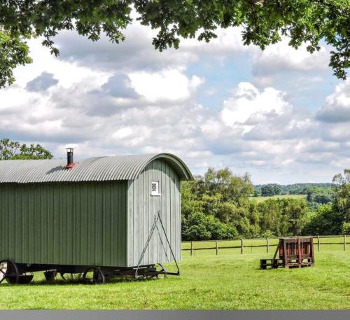 a green barn in the middle of a field at Skylark Shepherds Hut in Royal Tunbridge Wells