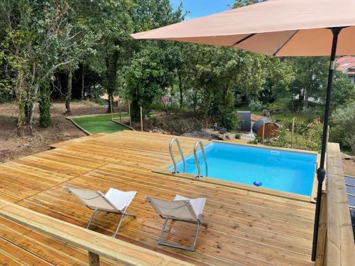 two chairs and an umbrella on a wooden deck with a pool at As casinhas do Moinho in Valença