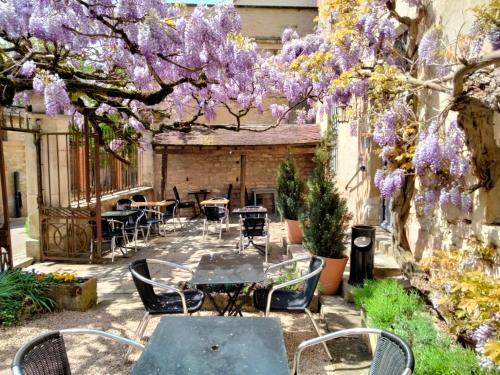 patio ze stołami, krzesłami i fioletowymi wisteriami w obiekcie Les Glycines Vézelay w mieście Vézelay