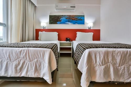 two beds in a hotel room with red walls at Ramada Hotel & Suites Campos Pelinca in Campos dos Goytacazes