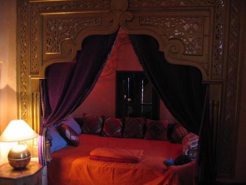 a bedroom with a red bed with a canopy at Riad Dar El Caid - Palais XIII Siecle in Tozeur