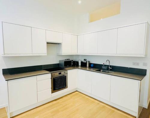 una cocina blanca con armarios blancos y fregadero en Spacious Flat, Fast WiFi, Free Parking, en Londres