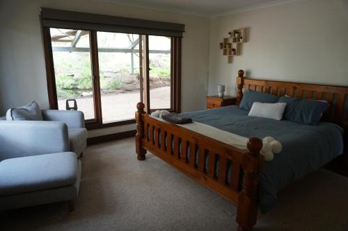 a bedroom with a bed and a chair and a window at Allusion Farmstay Cellar House Heated Pool - Fire Pit - Pizza Oven - Pool Table - Sleeps 16 in Yankalilla