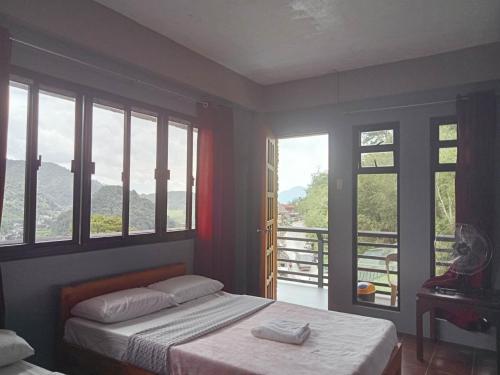 a bedroom with a bed and a balcony with windows at Banaue Pink Eco hostel in Banaue