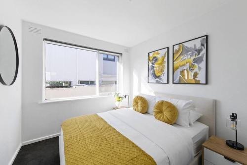 a white bedroom with a large bed with yellow pillows at Beachside Getaway on Selwyn in Melbourne