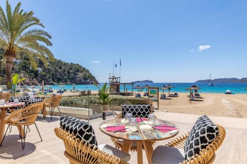 a patio with tables and chairs next to the beach at El Somni Ibiza Dream Hotel by Grupotel in Sant Joan de Labritja