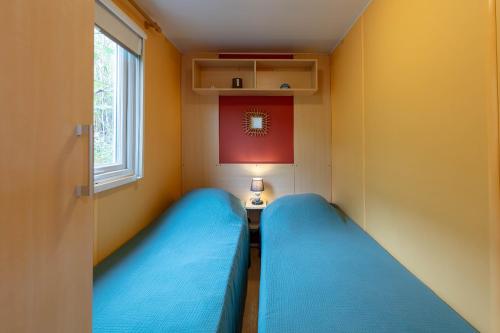 2 Betten in einem kleinen Zimmer mit Fenster in der Unterkunft L'Eucalyptus, mobil-home avec extérieur spacieux à quelques mètres de la mer in Hyères
