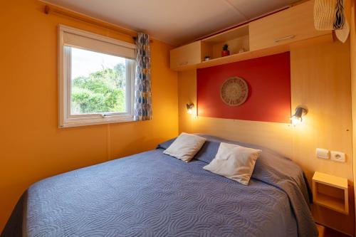 a bedroom with a blue bed and a window at L'Eucalyptus, mobil-home avec extérieur spacieux à quelques mètres de la mer in Hyères