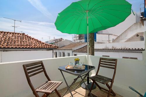 a table and two chairs with a green umbrella on a balcony at Casa da Avó Edite in Tavira