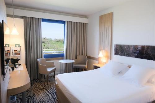 a hotel room with a bed and a desk and a window at Thalazur Ouistreham - Hôtel & Spa in Ouistreham