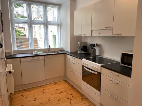 kuchnia z białymi szafkami, umywalką i oknem w obiekcie Frederiksberg Apartments 438 w Kopenhadze