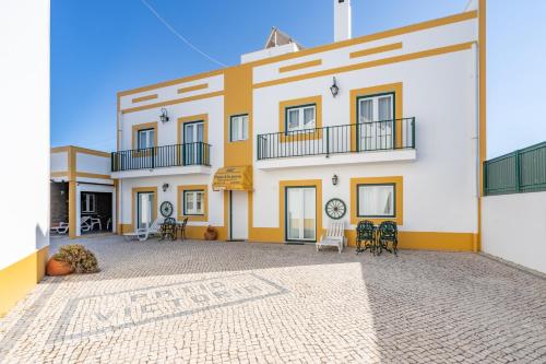 a large white and yellow building with chairs and tables at Apartamentos Pátio Victória by Umbral in Vila Nova de Milfontes
