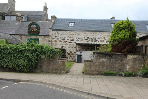 an old stone building with a garage and a driveway at Highlander Bunkhouse in Huntly