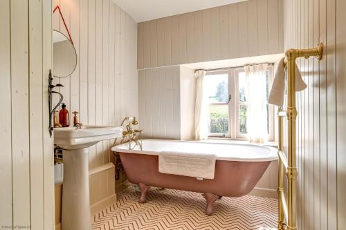 a bathroom with a tub and a sink and a window at Church End Cottage in Swerford