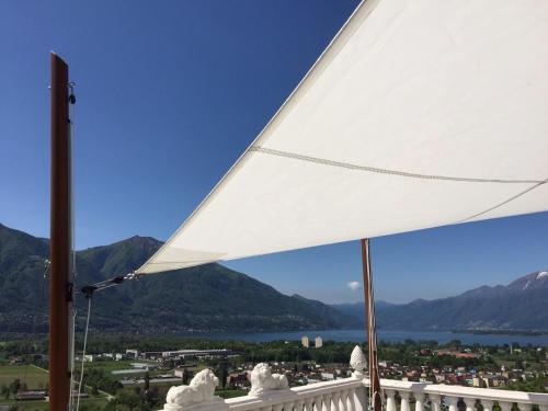 a white umbrella on top of a balcony with mountains at Ferienhaus Patrizia with a fantastic view of Lake Maggiore and the pool in Gordola
