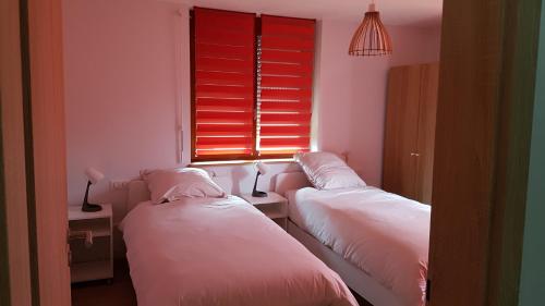 twee bedden in een kamer met een raam met rode jaloezieën bij Au chant de la rivière in Stosswihr