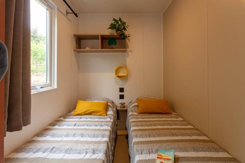 Duas camas num pequeno quarto com uma janela em Le Palmier, mobil-home sans vis-à-vis idéalement situé entre mer et vignes em Hyères