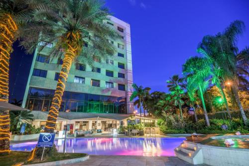 um hotel com piscina e palmeiras à noite em NH Cali Royal em Cali