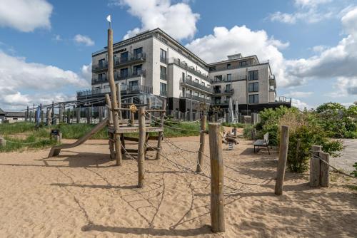 un parque infantil en la arena frente a un edificio en Küstenperle Strandhotel & Spa en Büsum