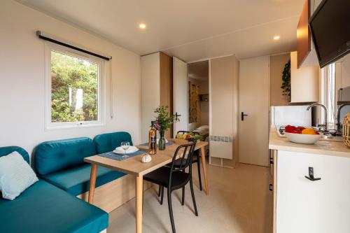 Una cocina y una sala de estar con una mesa y un sofá azul. en Le Cycas, mobil-home neuf avec sa vue dégagée sur les vignes et la mer, en Hyères
