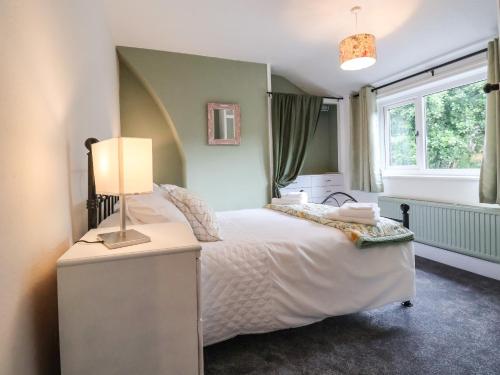 a bedroom with a bed with a lamp and a window at Gables Cottage in Northwich