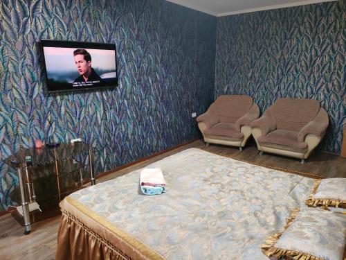 a room with a tv and a bed and two chairs at Glinki 33 Apartments in Semey