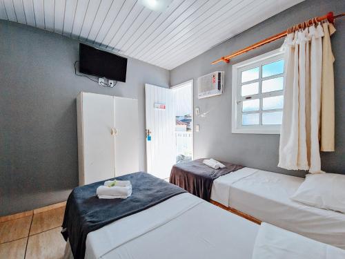 two beds in a room with a tv and a window at Pousada Água Marinha in Cabo Frio