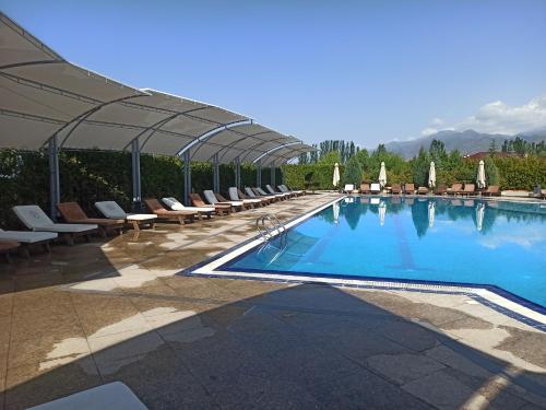 a large swimming pool with lounge chairs and an umbrella at Иссык-Куль ЦО "Karven Four Seasons" таунхаус in Chon-Sary-Oy