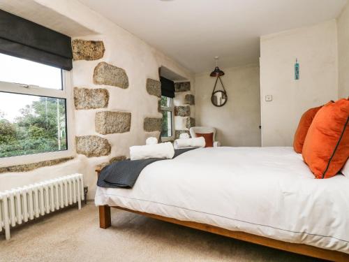 a bedroom with a white bed and a stone wall at Kilden Cottage in Helston