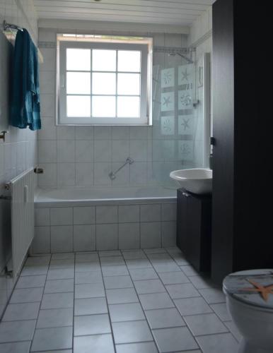baño con bañera, lavabo y ventana en Schoner im Schiffehaus, en Wangerland