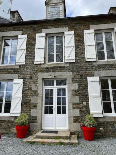 a brick house with white doors and two potted plants at La Maison des Amis en Normandie in Pontfarcy