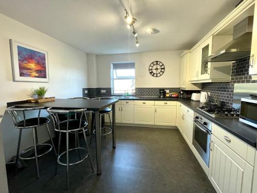 a kitchen with white cabinets and a table with stools at Apartment 3 Benllech with Sea views in Benllech
