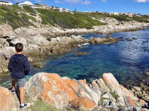 a boy standing on a rock looking at the water at Self Catering Apartment - De Kelders in De Kelders