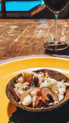 a bowl of food on a yellow plate with a wine glass at Pousada Vila do Alto in Japaratinga