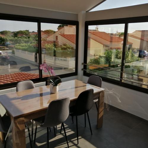 une salle à manger avec une table, des chaises et des fenêtres dans l'établissement location maison de vacances jusqu'à 6 personnes près du port et de la plage, au Barcarès