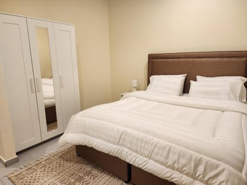 ein Schlafzimmer mit einem großen Bett mit weißer Bettwäsche und einem Spiegel in der Unterkunft Nesaj Villa in Dammam