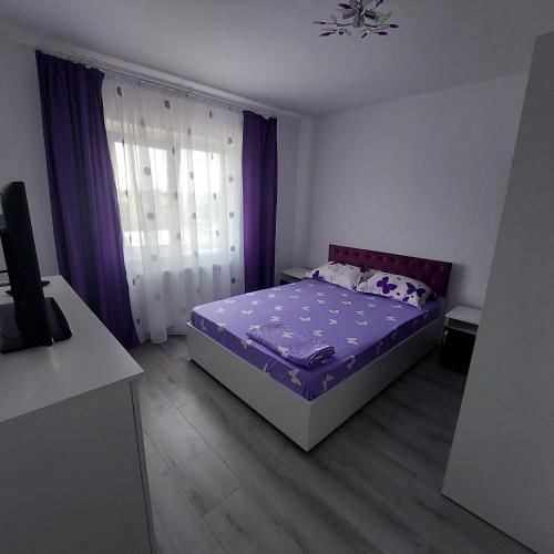 ein Schlafzimmer mit einem Bett mit violetter Bettwäsche und violetten Vorhängen in der Unterkunft Apartament Sara in Bîrlad