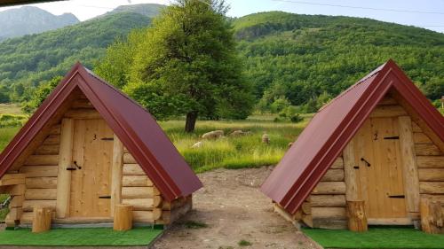 two wooden huts in a field with mountains in the background at Bungalows Malagić in Gusinje