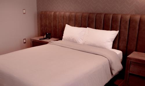a bedroom with a white bed with a wooden headboard at Hotel Capitalino in Pachuca de Soto