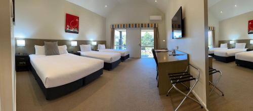 a hotel room with four beds and a desk at Brooklands Of Mornington in Mornington