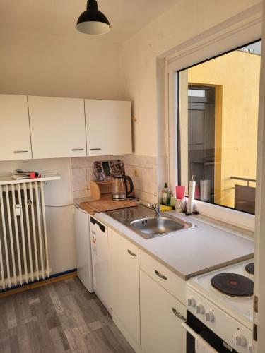 cocina con armarios blancos, fregadero y ventana en FEE Apartment 1 Bremerhaven, en Bremerhaven